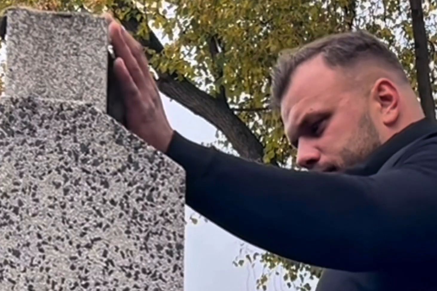 Filip Szczepański opiera dłoń o granitowy słup i przygląda się kamieniowi