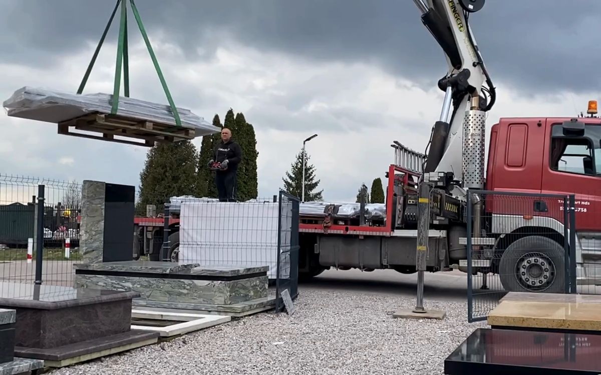 Dźwig podnosi płytę nagrobka z samochodu
