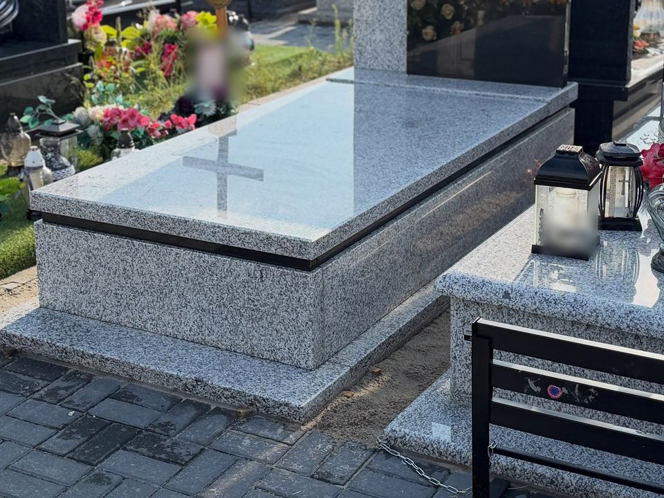 Jasny granitowy nagrobek z czarną listwą, w płycie odbija się krzyż